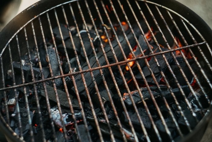 A close-up of a rusty old barbeque grill with burning charcoal underneath it.