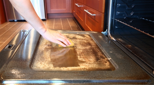 A close up of a person cleaning an oven door with a sponge